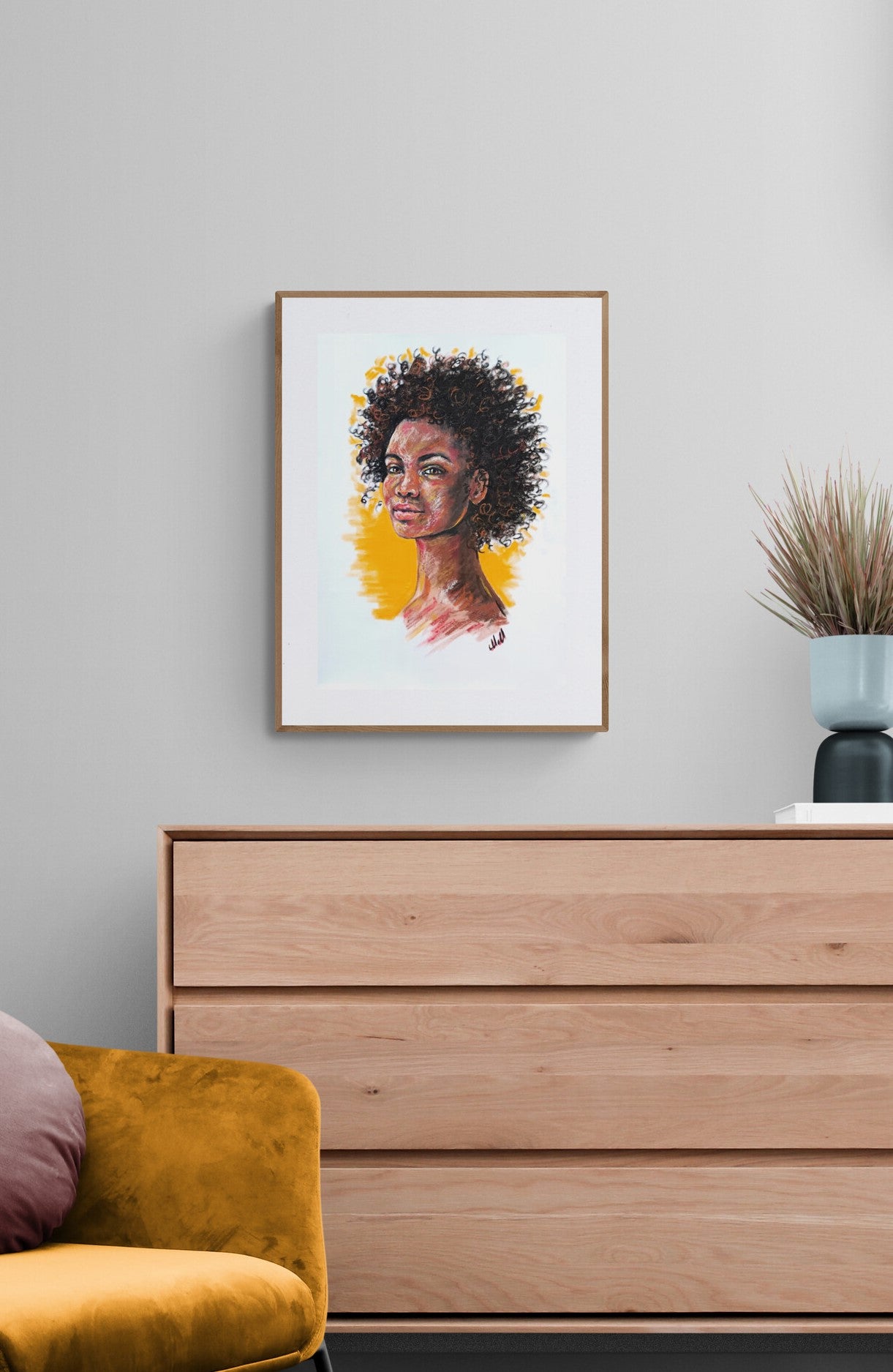 Framed artwork of a woman's portrait above a wooden dresser with a yellow chair and plant.