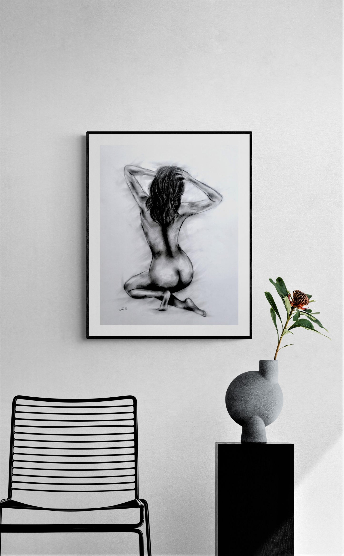 Framed black and white artwork of a nude figure on a wall above a chair.