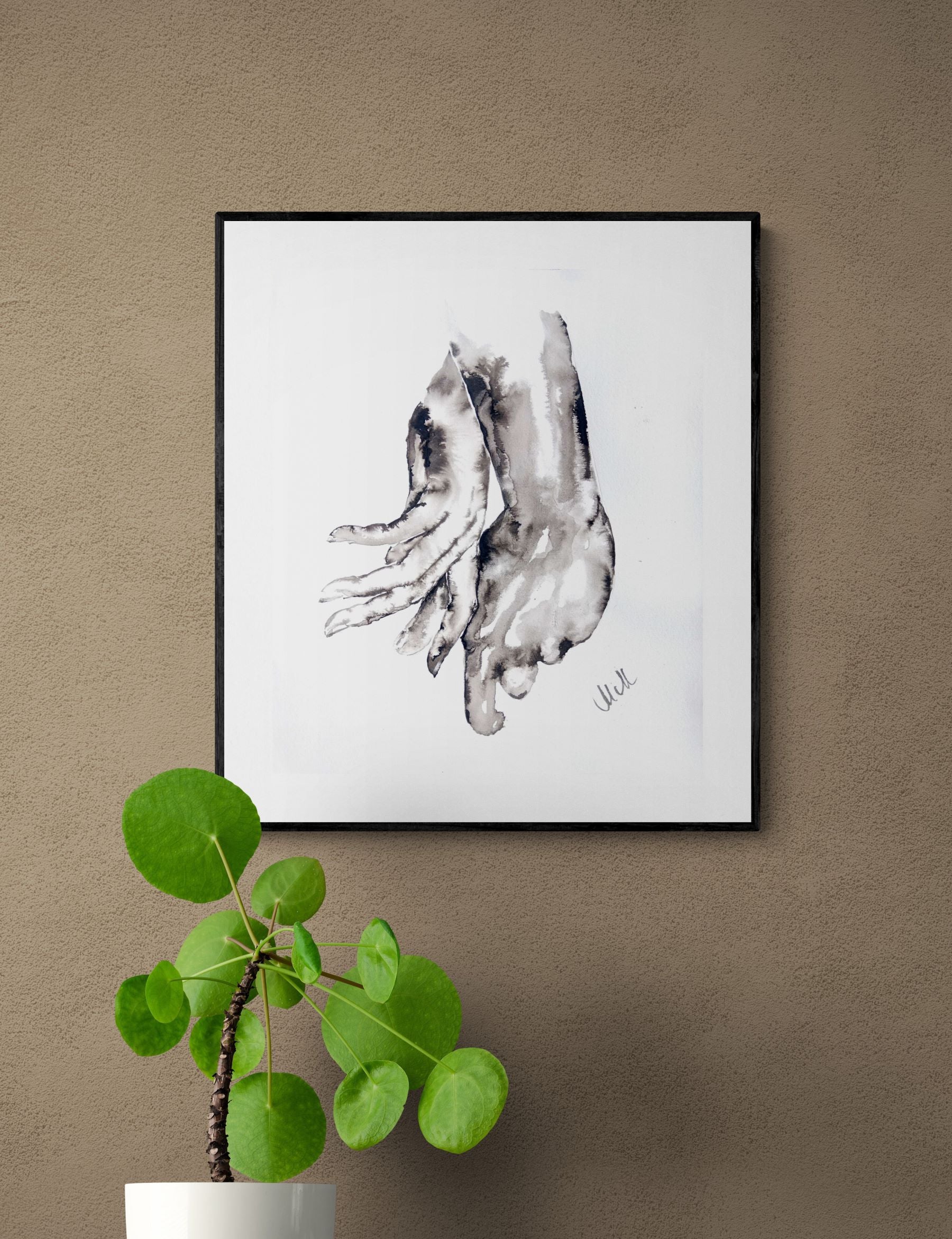 Framed black and white artwork of a foot on a beige wall with a potted plant below.