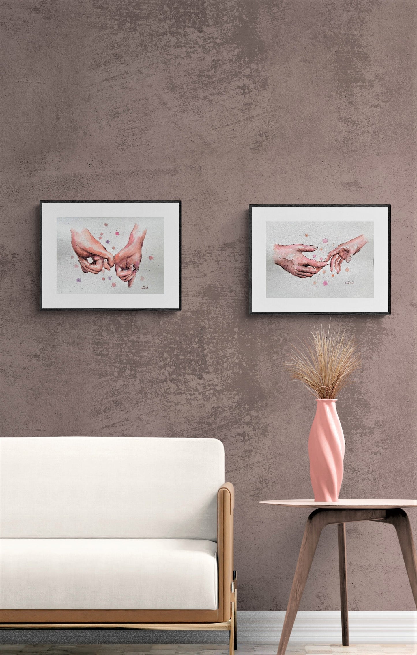 Two framed artworks on a textured wall above a white sofa with a pink vase on a table.