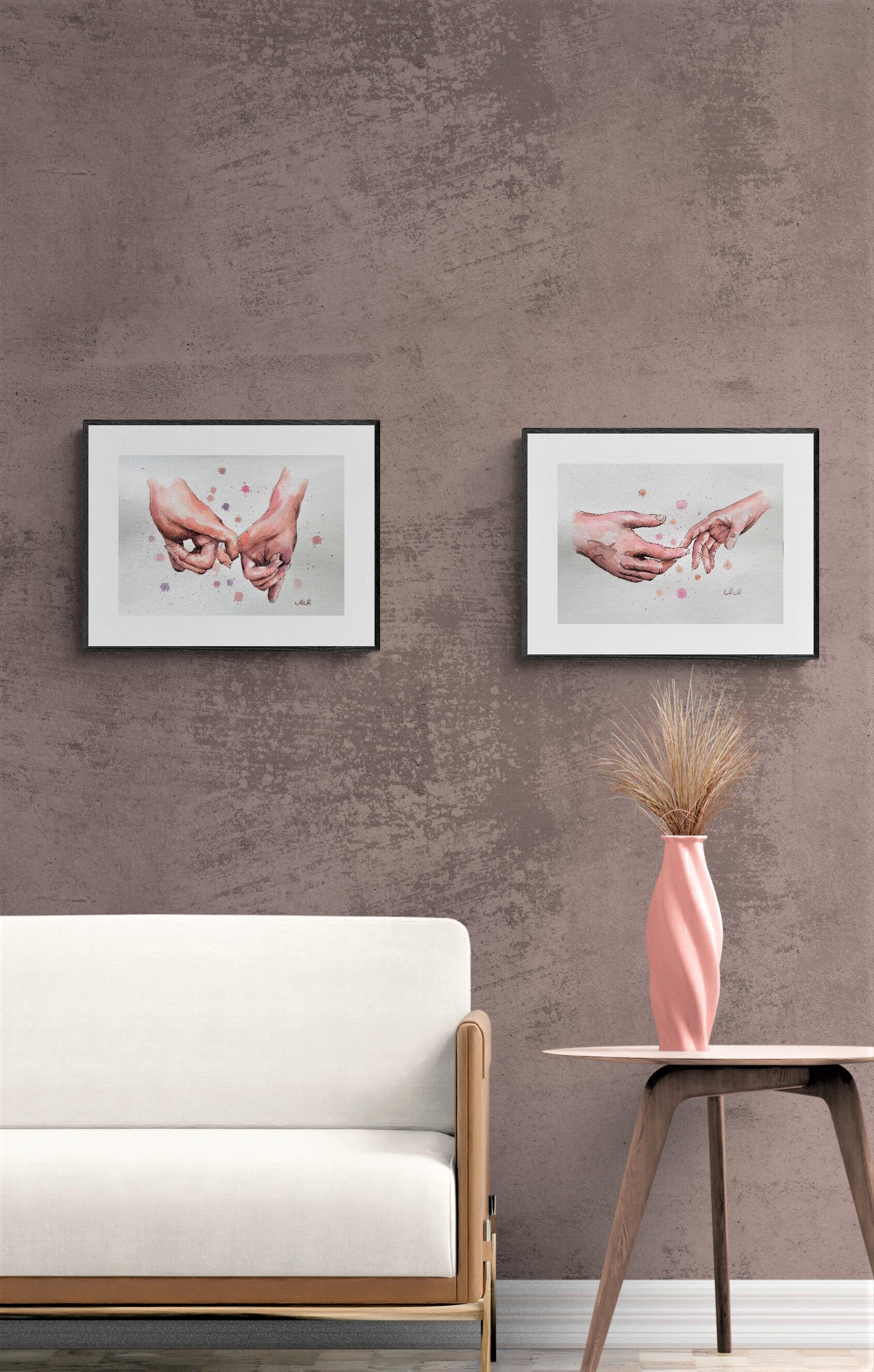 Two framed artworks on a textured wall above a white sofa with a pink vase on a table.