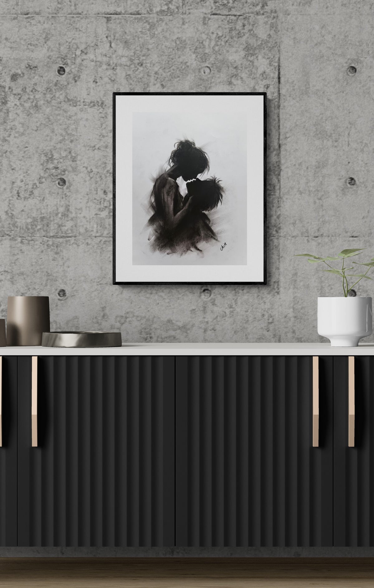A framed black and white art print depicting an embracing couple, displayed on a textured gray concrete wall above a modern dark gray ribbed console cabinet with gold handles.