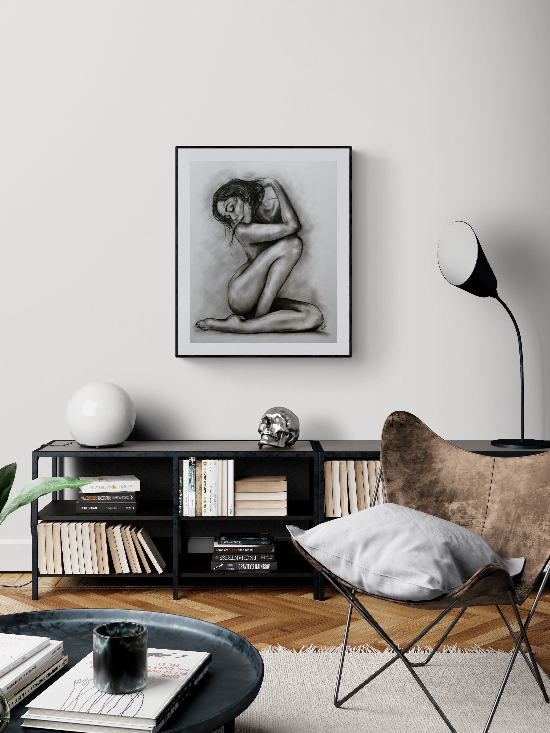 Modern living room with a black and white framed artwork on the wall, a black shelf with books and decor items, and a brown chair.