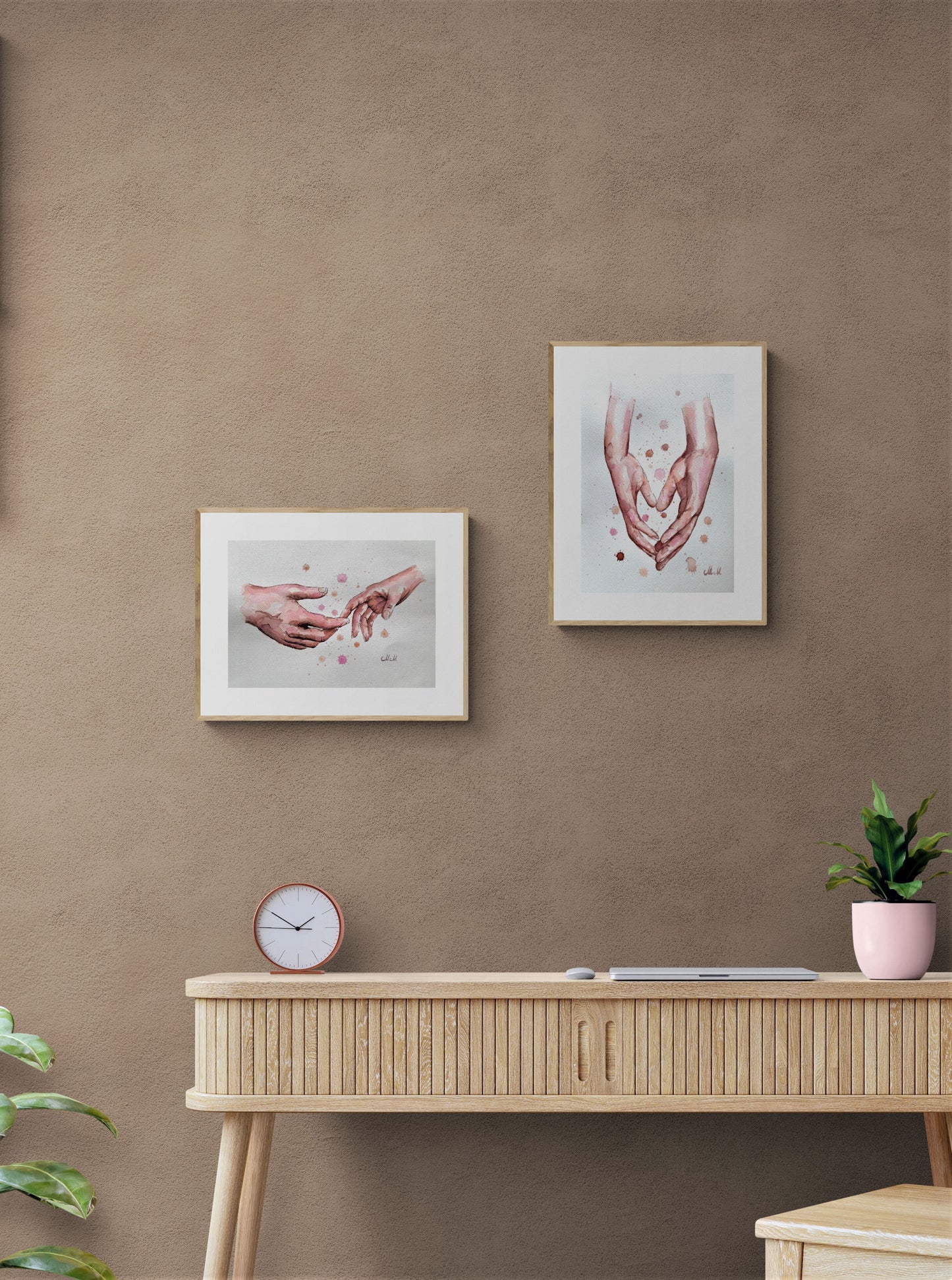 Two framed artworks on a brown wall above a wooden desk with a clock and plant.