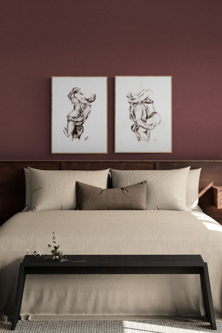 A styled bedroom scene with a bed dressed in beige bedding and pillows, set against a deep burgundy wall. Above the bed are two framed abstract sketches.
