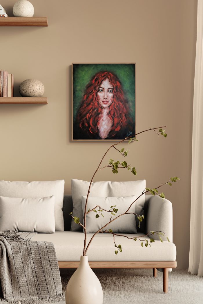 A framed portrait painting of a woman with vibrant red hair and a green background, displayed on a beige wall above a modern white sofa in a styled living room.