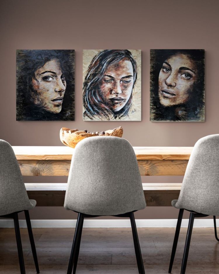 A three-panel canvas wall art set depicting expressive portraits of three women, displayed in a dining room setting above a wooden table and gray chairs.