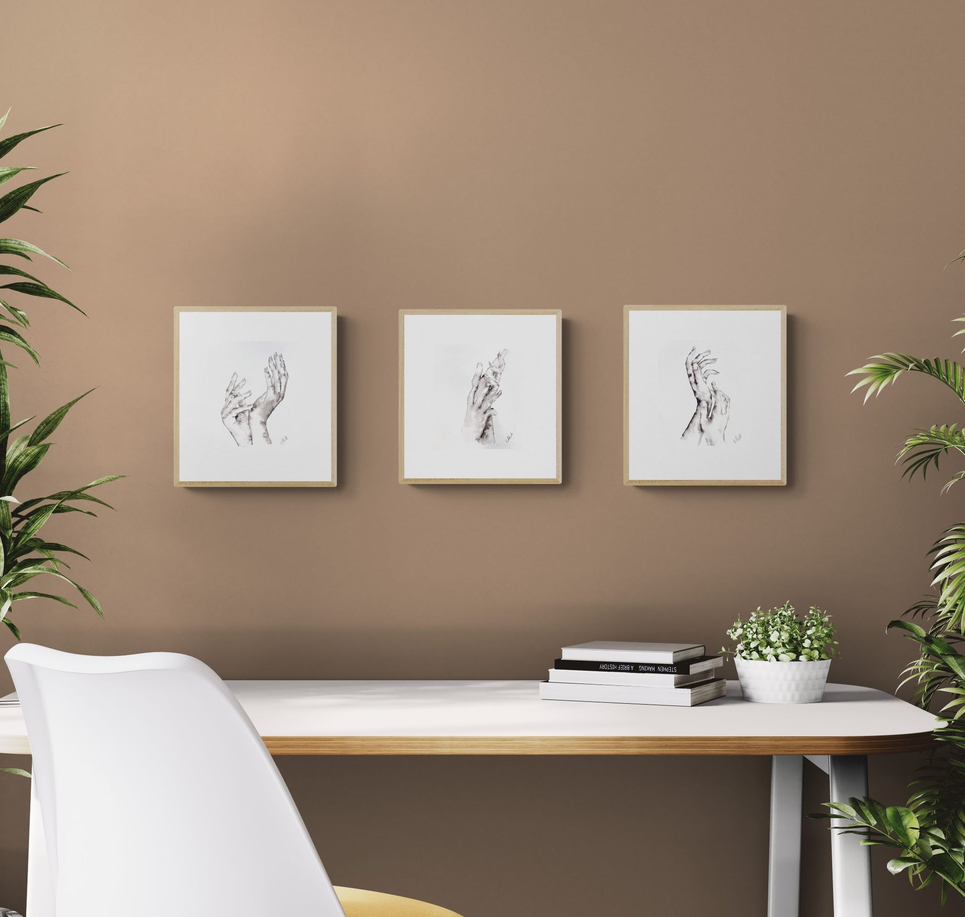 Three framed artworks on a brown wall above a desk with books and a plant.