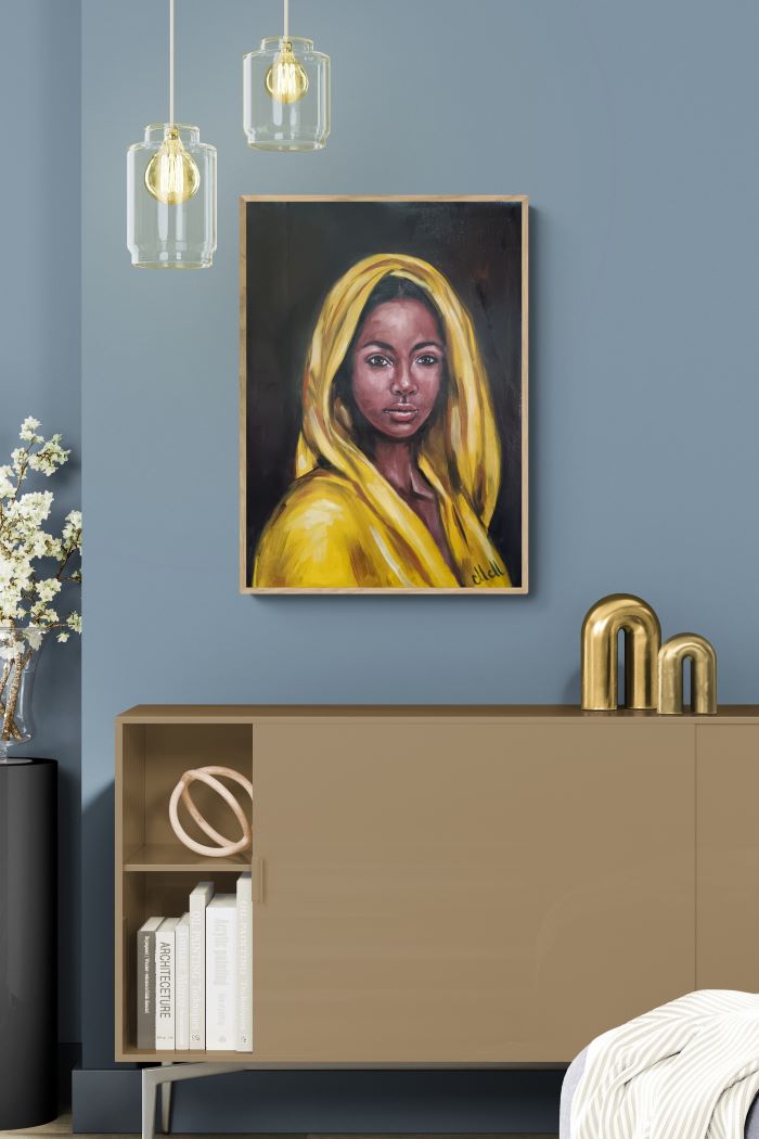 A framed portrait painting of a woman in a bright yellow headscarf hanging on a blue-gray wall above a beige sideboard, with pendant lights and decorative gold objects in the room.