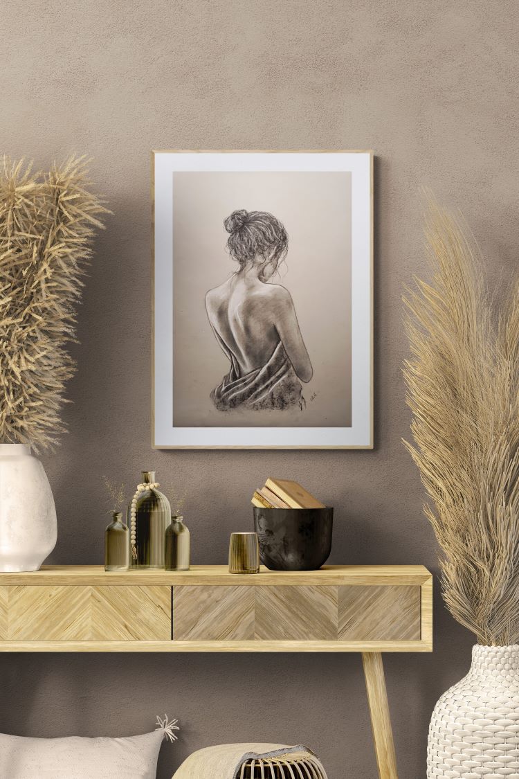 A framed monochrome sketch print of a woman's back hangs on a textured taupe wall above a light wood console table styled with dried grasses and decorative bottles.