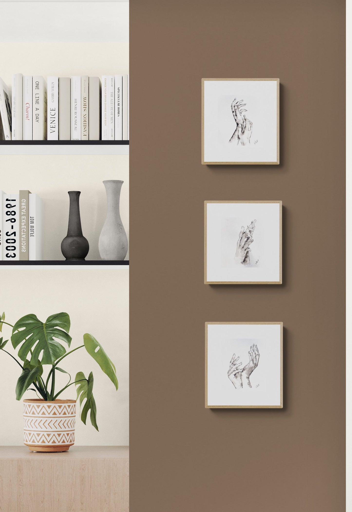 Three framed artworks on a brown wall with a shelf and plant in the background.
