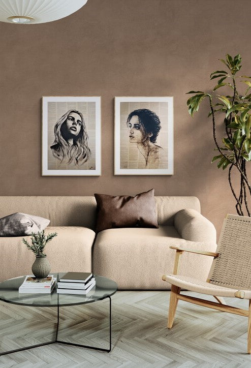 Two framed black and white portrait sketches of women hanging on a warm taupe wall above a beige sofa in a styled living room.