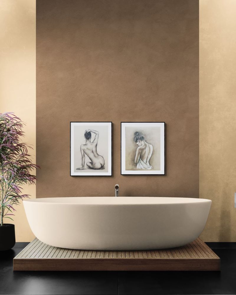 A modern freestanding oval bathtub placed on a wooden platform in a bathroom setting, with two framed art prints on a textured brown wall behind it and a potted plant at the side.