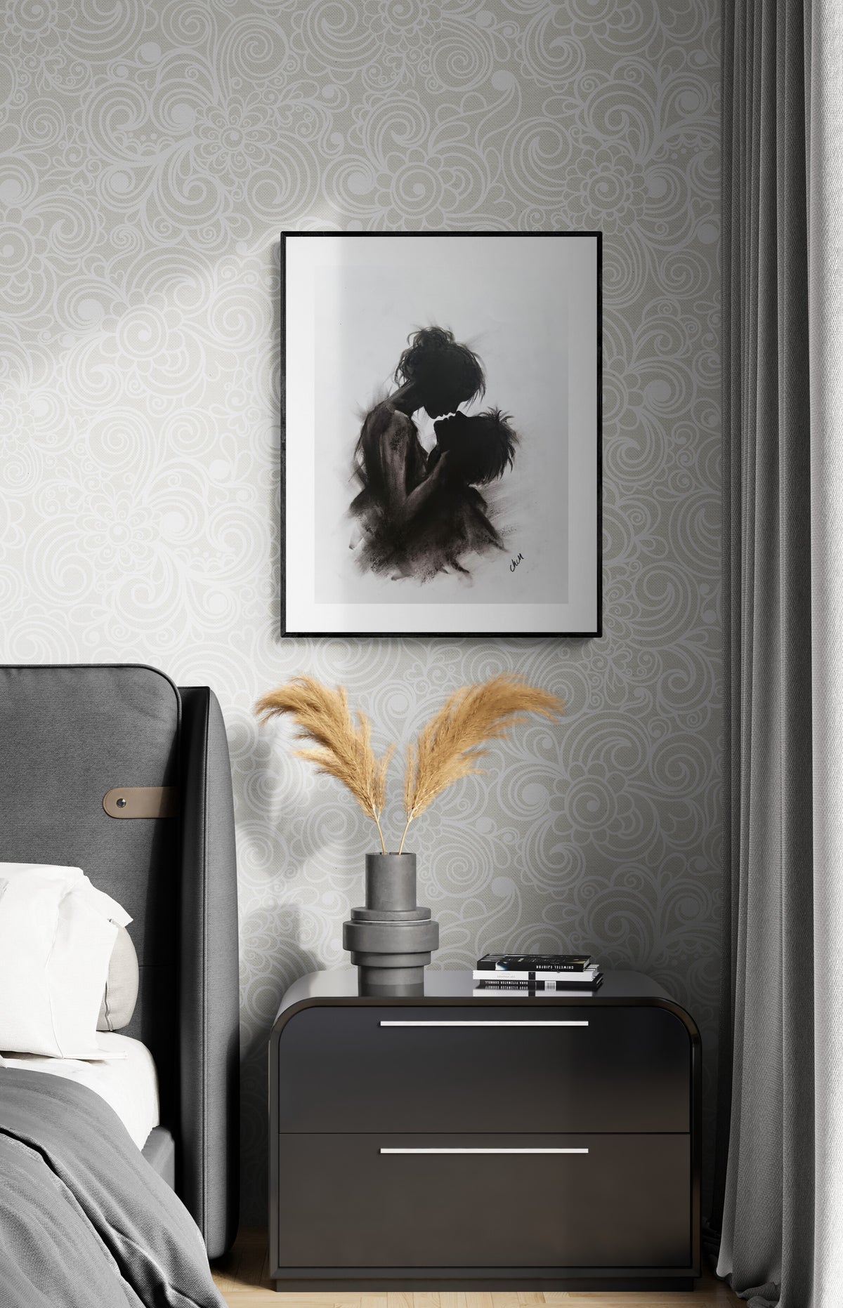 A framed black and white art print of an embracing couple hangs on a gray patterned wallpaper wall above a dark gray nightstand with a vase of pampas grass in a modern bedroom setting.