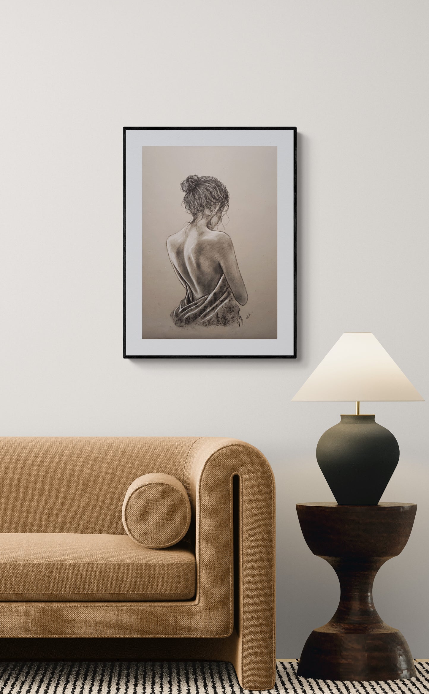 Framed artwork of a woman on a wall above a beige sofa with a lamp on a side table.